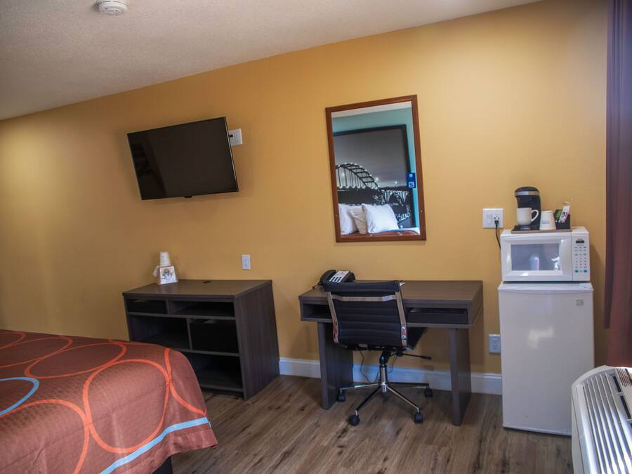 A hotel room with a bed, desk, chair, television, and a refrigerator.