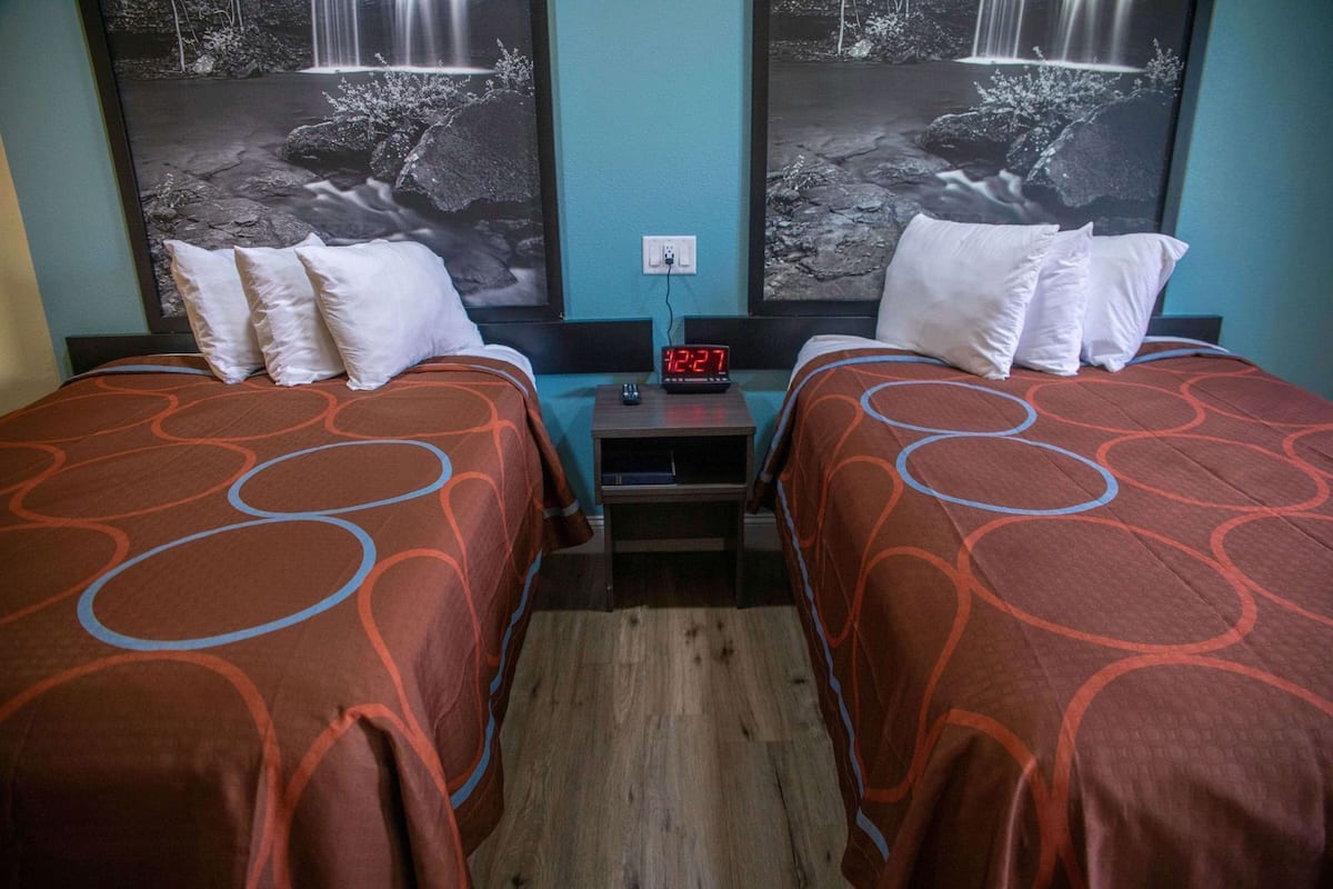 A hotel room with two beds, a nightstand with a clock, and two large wall-mounted pictures of waterfalls.