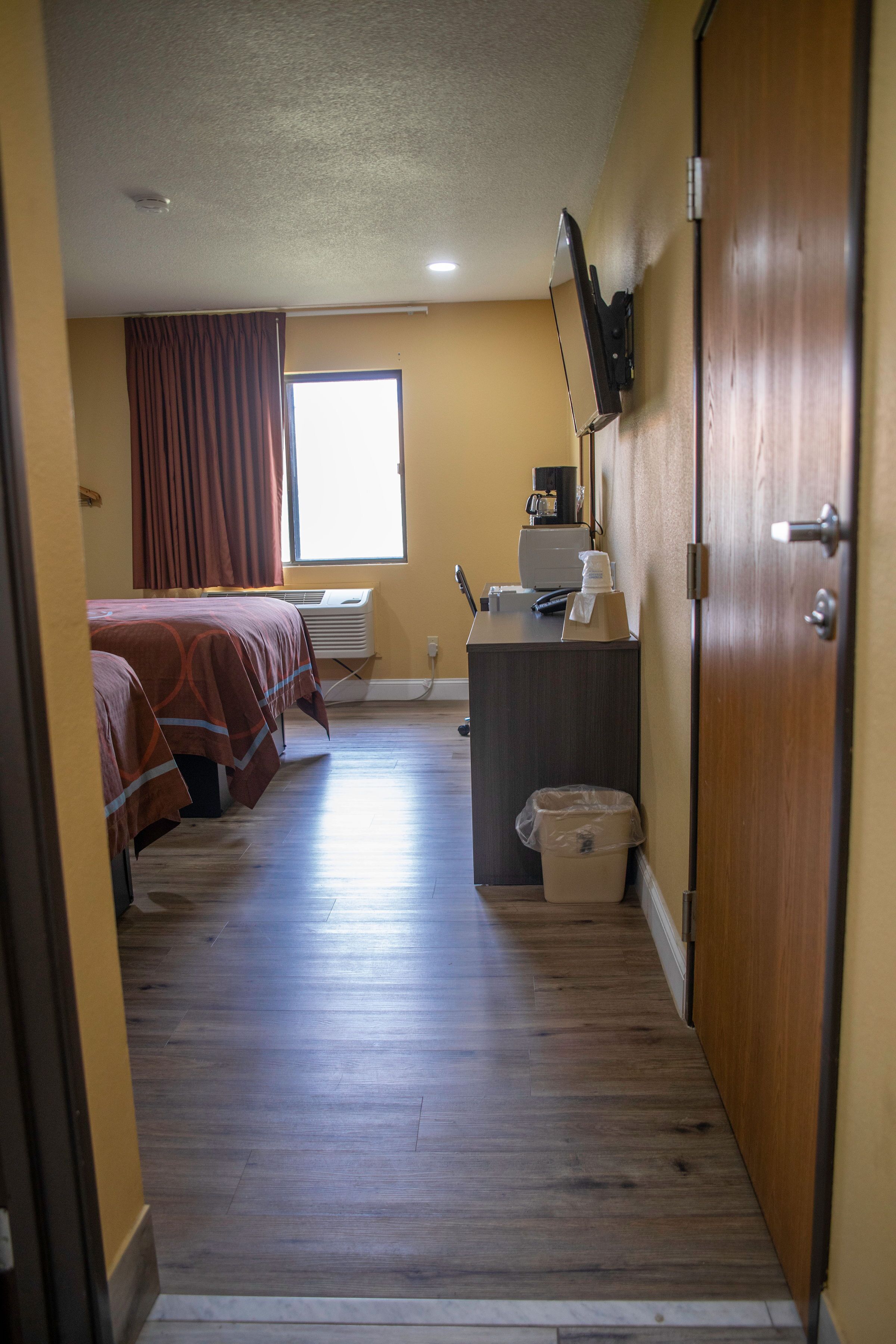 A hotel room with two beds, a desk with a computer, an air conditioner, and a window with curtains.