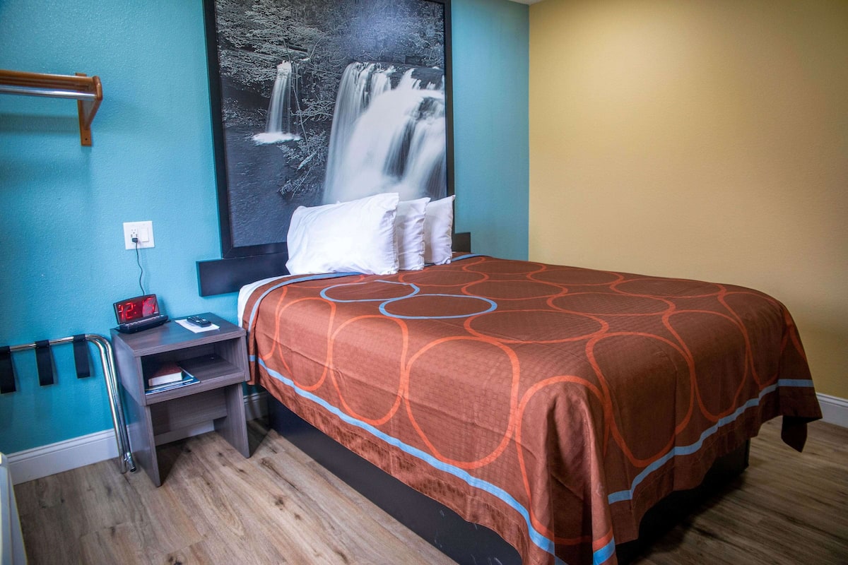 A hotel room with a bed, a nightstand, a wall-mounted clock, and a large poster of a waterfall.