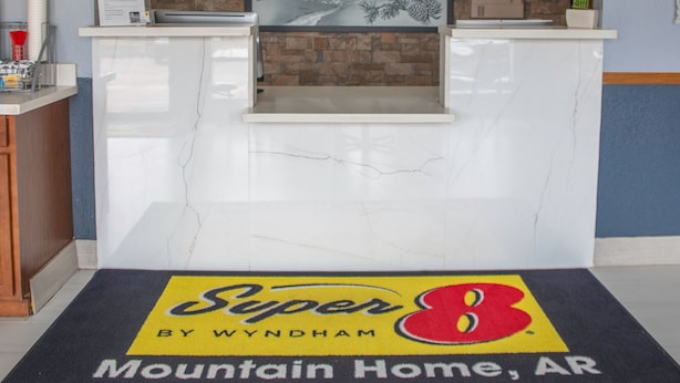 Un espace d’accueil doté d’un comptoir en marbre, d’une pancarte d’accueil encadrée et du logo Super 8 by Wyndham sur le tapis d’entrée.