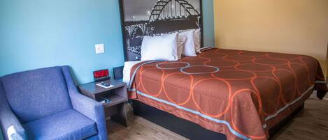 A hotel room with a bed, a chair, a nightstand, and a wall art of a bridge.