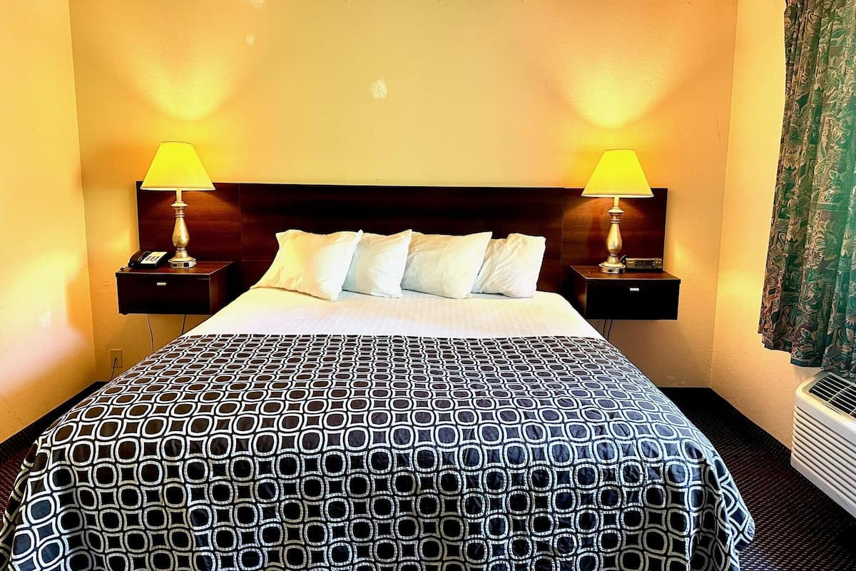 A hotel room with a large bed, two bedside tables with lamps, a headboard, and a window with curtains.
