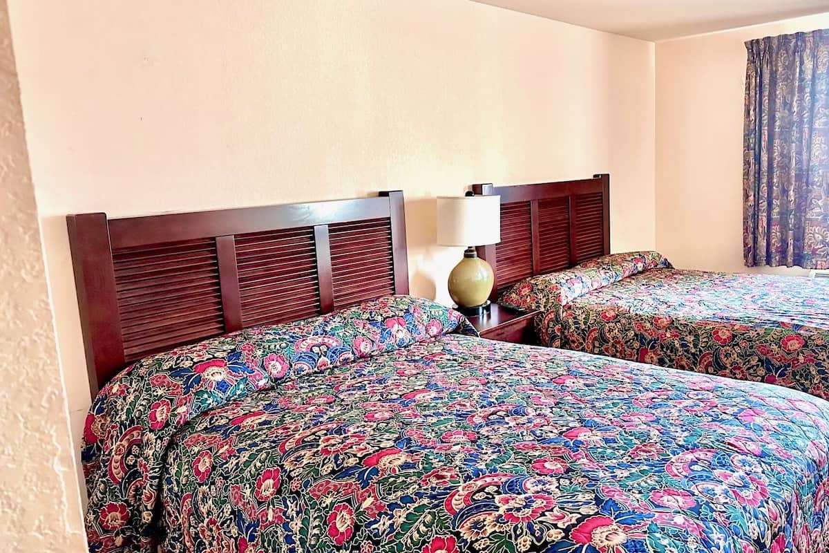 A hotel room with two beds, a wooden headboard, a lamp, and a window with curtains.