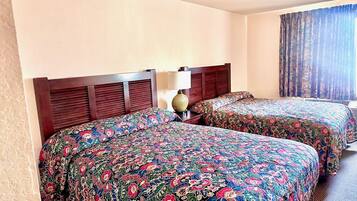 A hotel room with two beds, a wooden headboard, a lamp, and a window with curtains.
