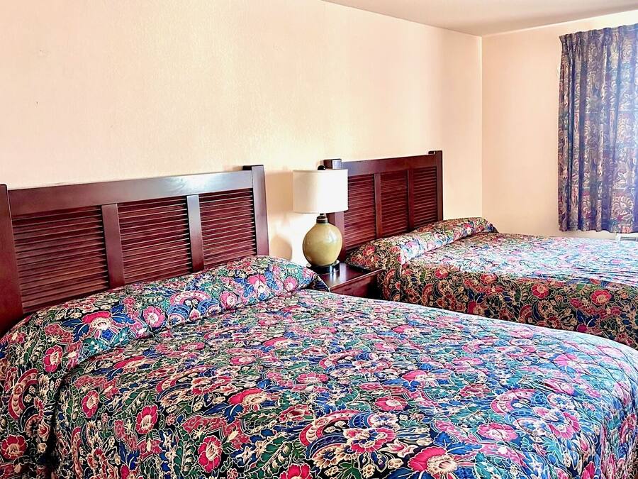 A hotel room with two beds, a wooden headboard, a lamp, and a window with curtains.
