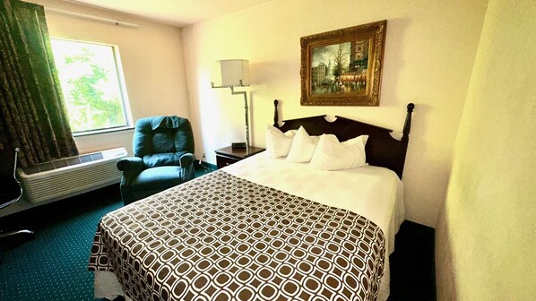 Habitación de hotel con cama, una silla, una lámpara, un cuadro y una ventana con cortinas.