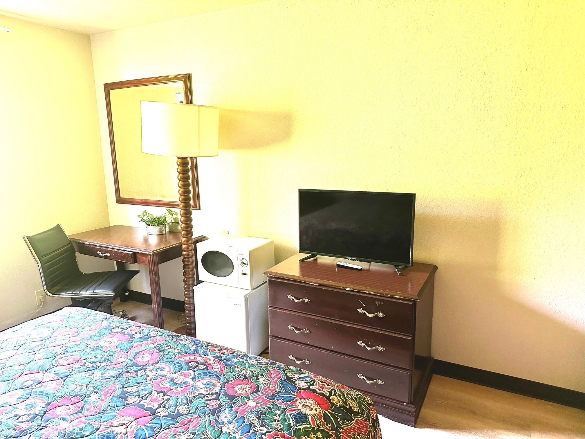 A hotel room with a bed, a desk, a television, a dresser, and a lamp.