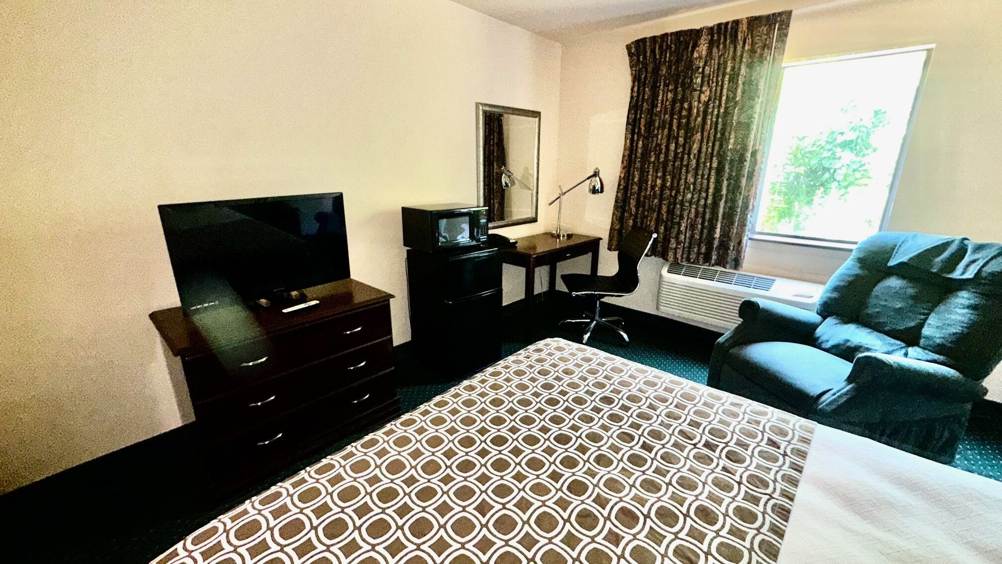 A hotel room with a bed, a television, a desk, a chair, and a window with curtains.