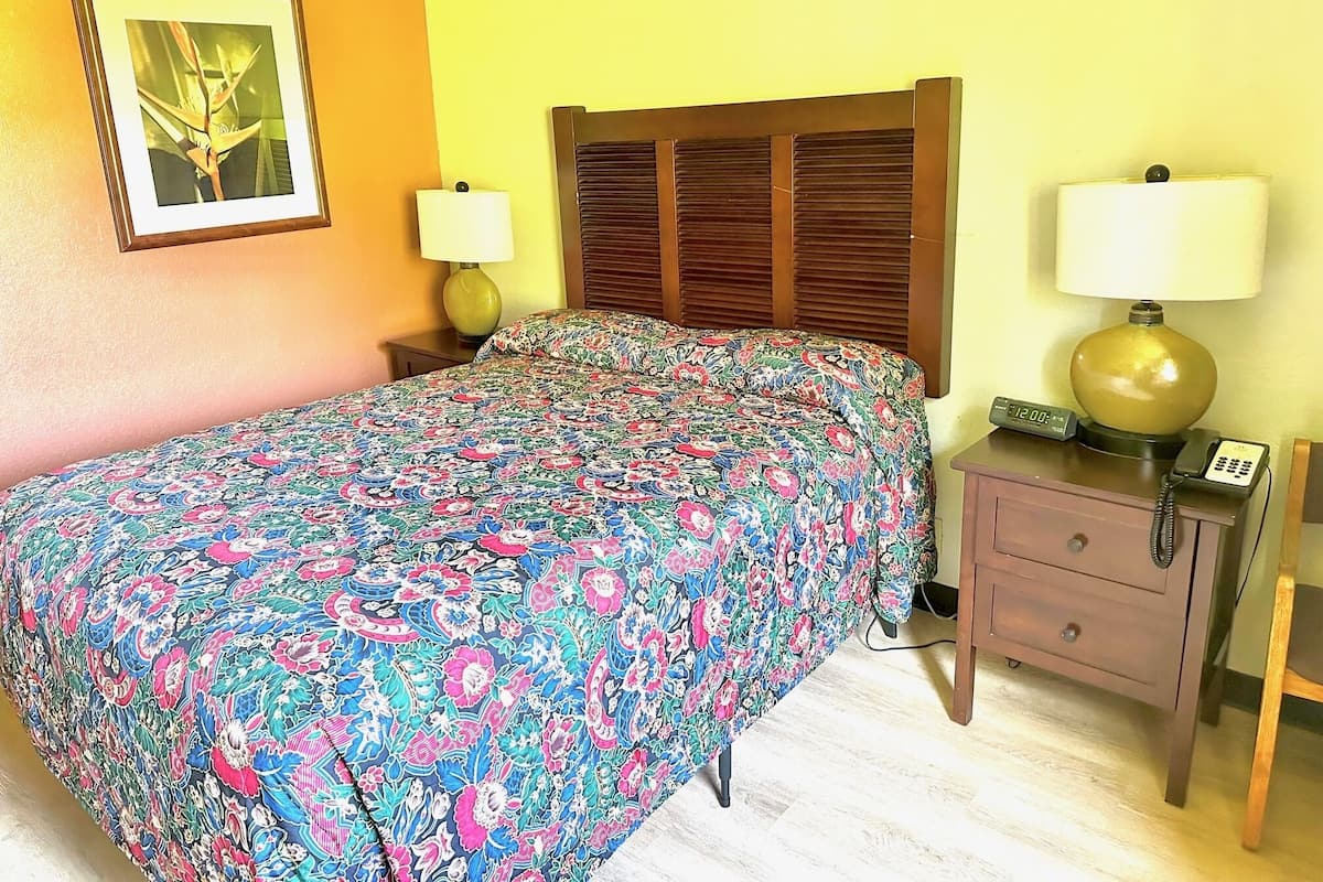 A bedroom with a floral bedspread, a wooden headboard, a bedside lamp, a nightstand, and a telephone.
