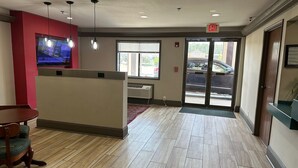 A hotel lobby with a reception desk, a television, and a fire exit. - Haven Inn & Suites (Monroe)