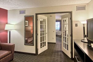 A hotel room with a carpeted floor, a chair, a desk with a lamp, and a television.