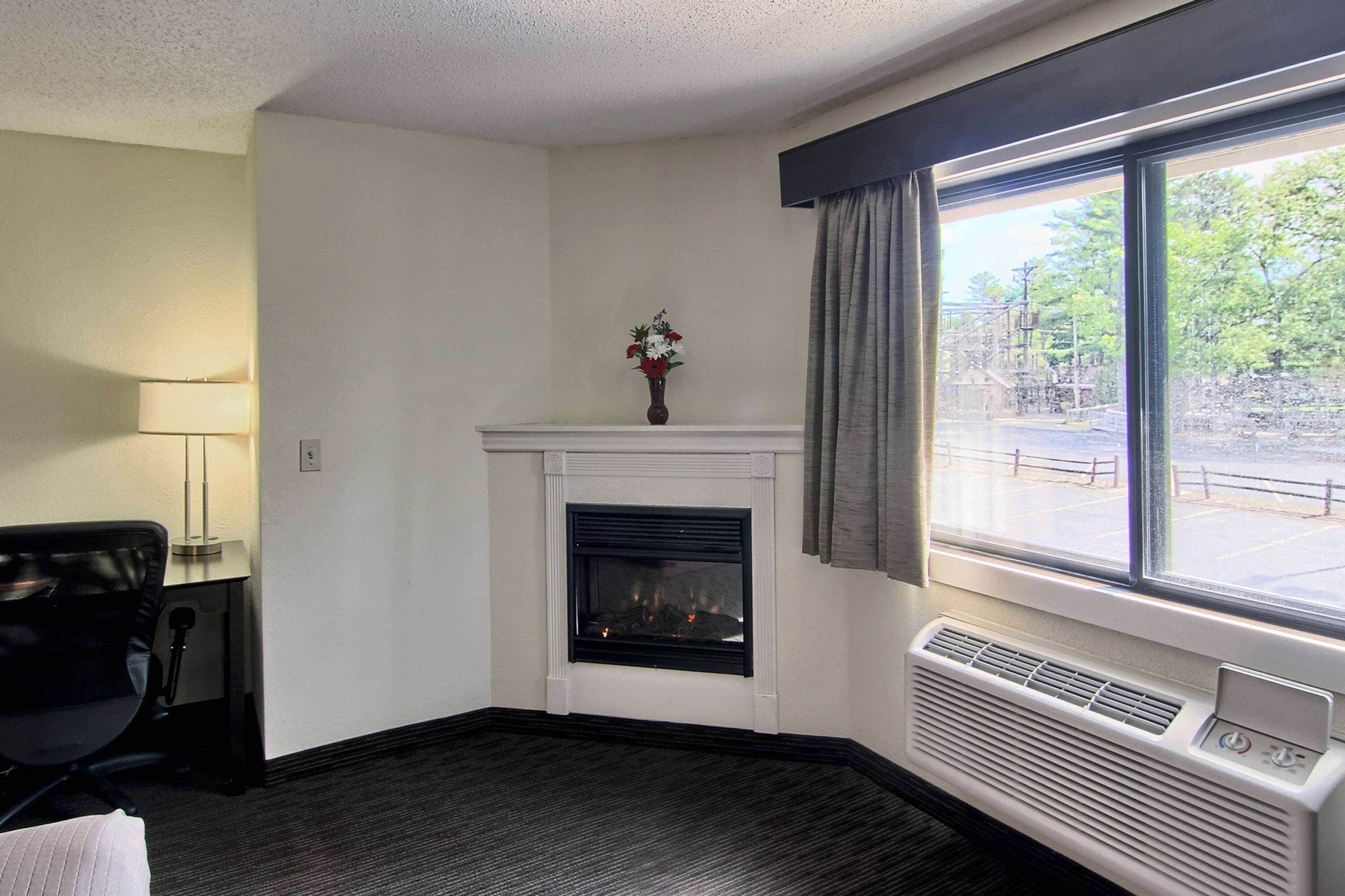 Habitación de hotel con chimenea, un escritorio con lámpara y ventana con vista al exterior.