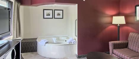 A hotel room with a large bathtub, a television, a sofa, and a lamp.