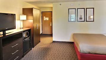 Habitació d'hotel amb un llit, televisió, microones, nevera i una porta que dona a un passadís.
