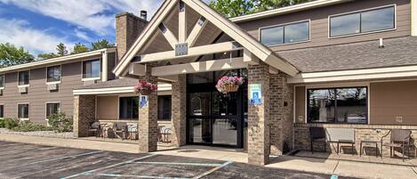 A hotel entrance with a covered patio, outdoor seating, and a parking lot.