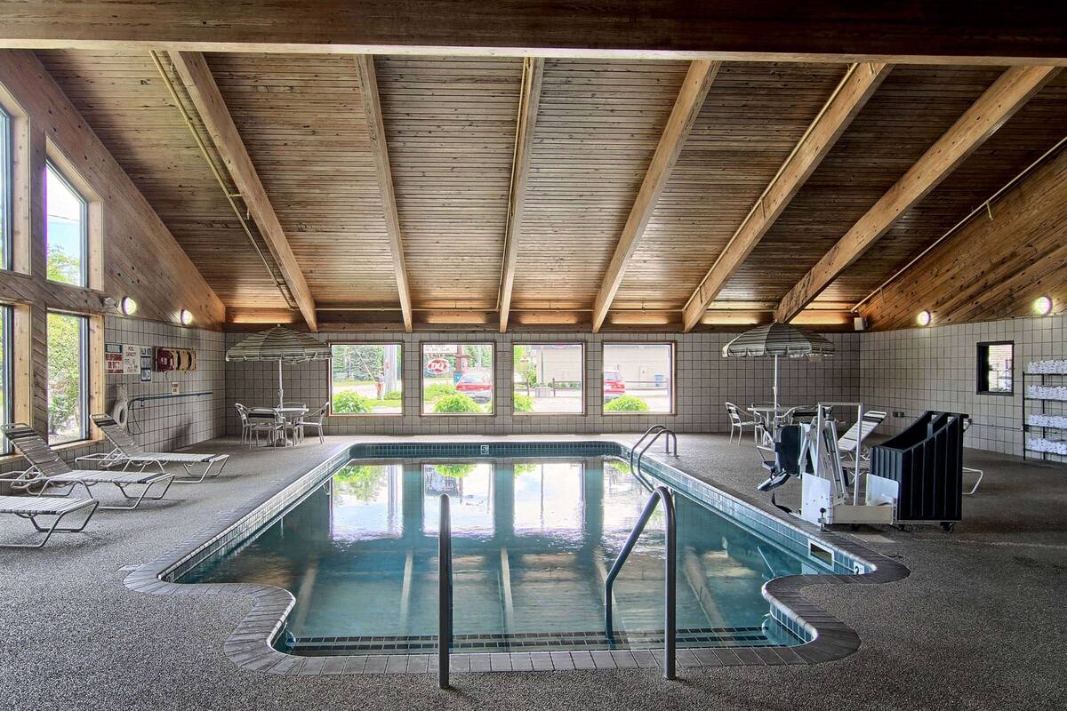 An indoor swimming pool with wooden beams, tiled walls, and lounge chairs.