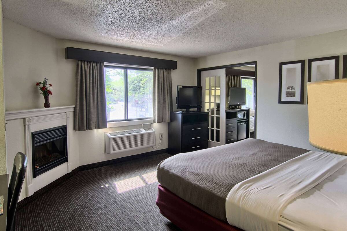 A hotel room with a fireplace, a television, a desk, and a bed.