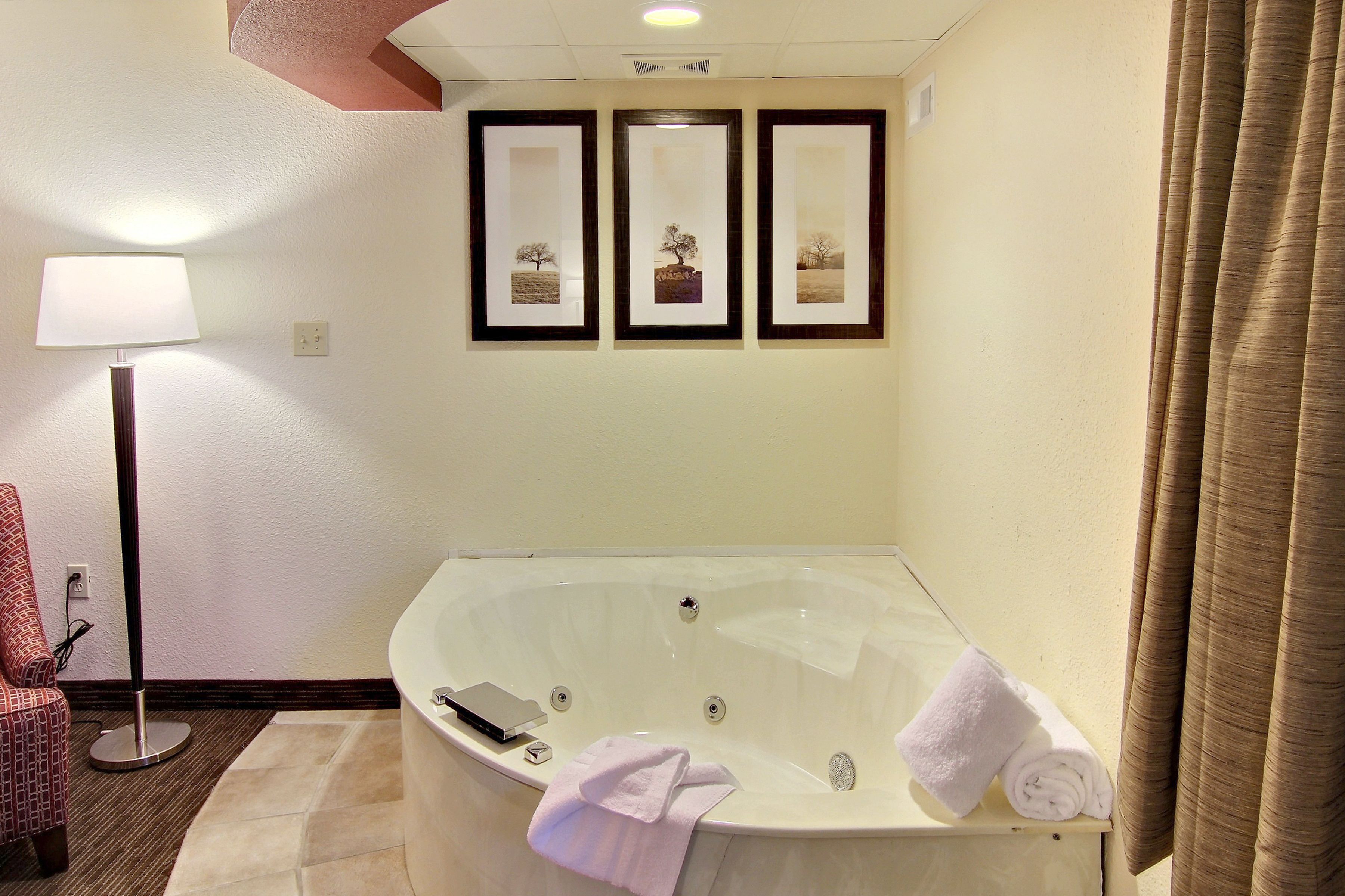 Un baño con una bañera grande, una lámpara de pie y cuadros en la pared.