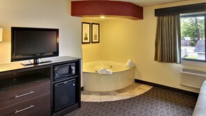 Quarto de hotel com televisão de tela plana, banheira de canto e quadros nas paredes.