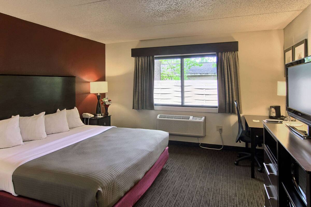 A hotel room with a large bed, a desk with a computer, a TV, and a window with curtains.