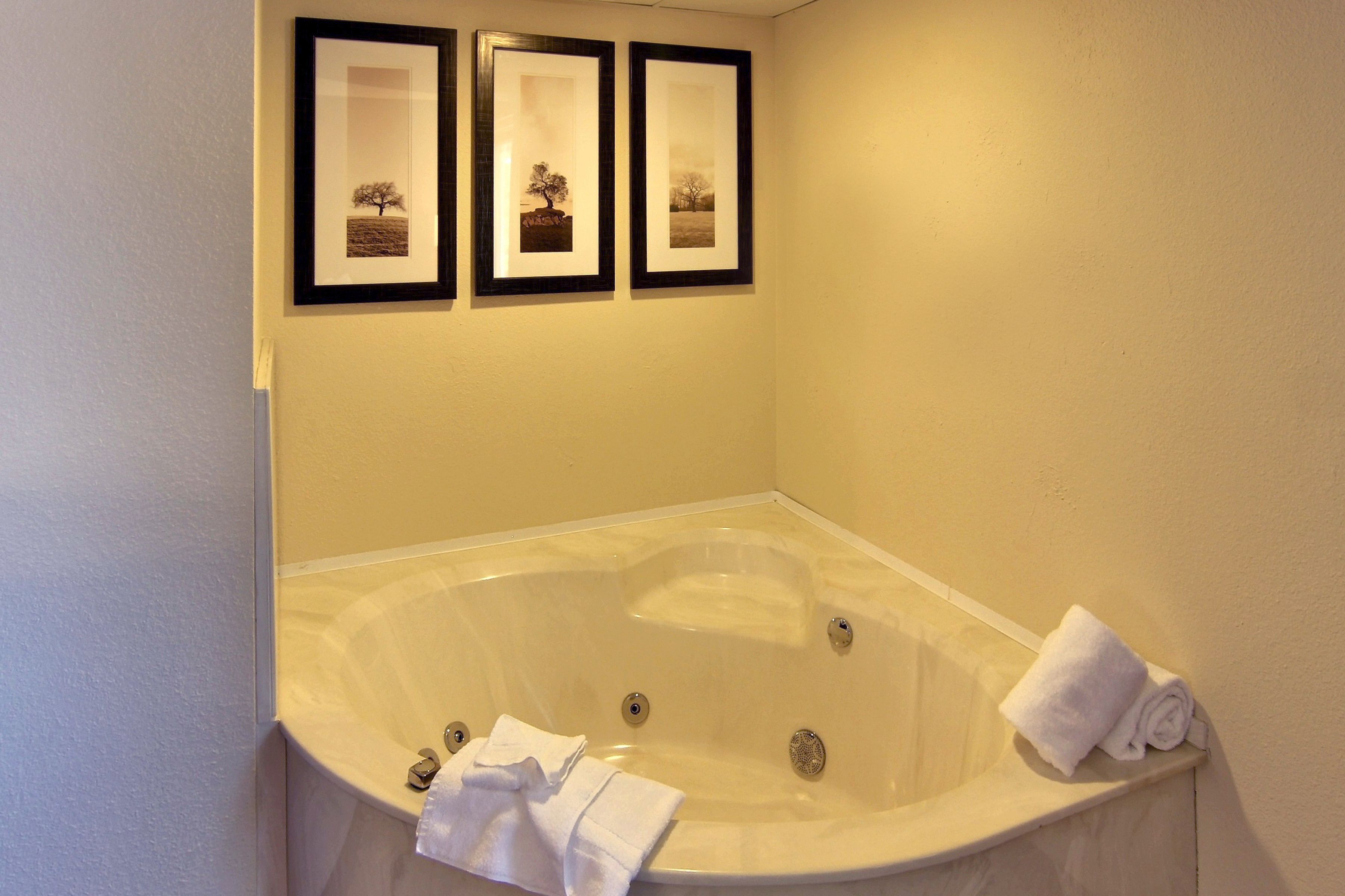 Une salle de bain avec une baignoire sur pieds, des tableaux encadrés accrochés au mur et une serviette roulée posée sur le bord.
