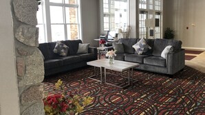 A lobby with a stone wall, two grey sofas with patterned cushions, a coffee table, and a colorful carpet. - HomeTown Inn & Suites (Belle Plaine)