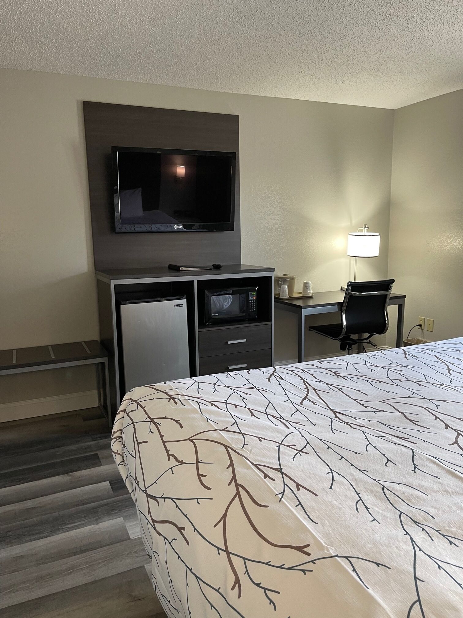 Una habitación de hotel con una cama, un escritorio con computadora, televisor, microondas y una lámpara.