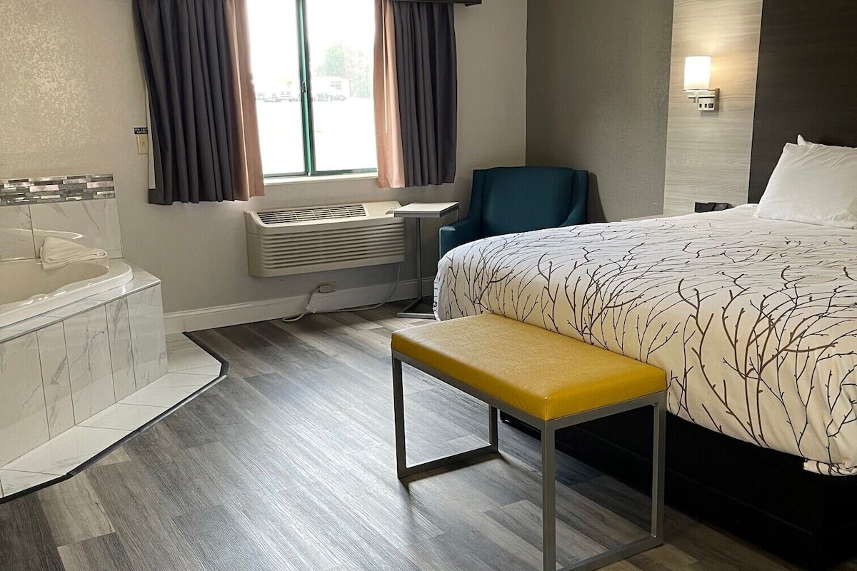 A hotel room with a bed, a bench, a chair, a desk, and a window with curtains.