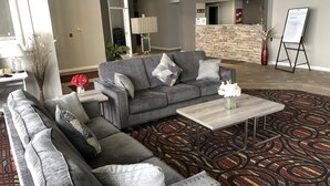 A modern lobby with grey sofas, a patterned carpet, and a reception desk. - HomeTown Inn & Suites (Belle Plaine)