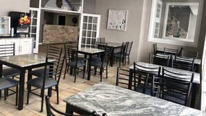 A restaurant with multiple dining tables and chairs, a kitchen area, and a stone wall. - HomeTown Inn & Suites (Belle Plaine)