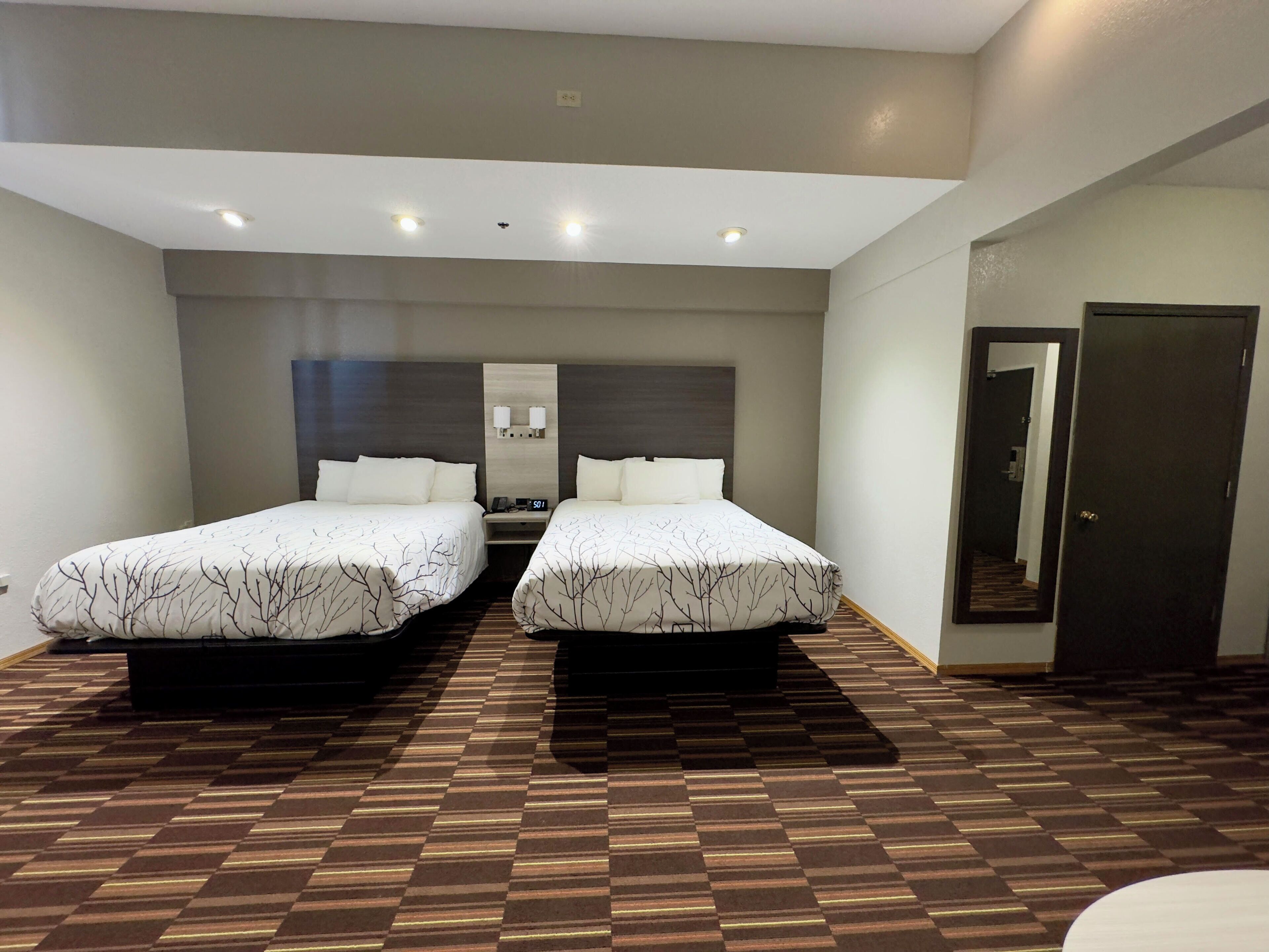 Habitación de hotel con dos camas, una mesita de noche, un espejo y una puerta.