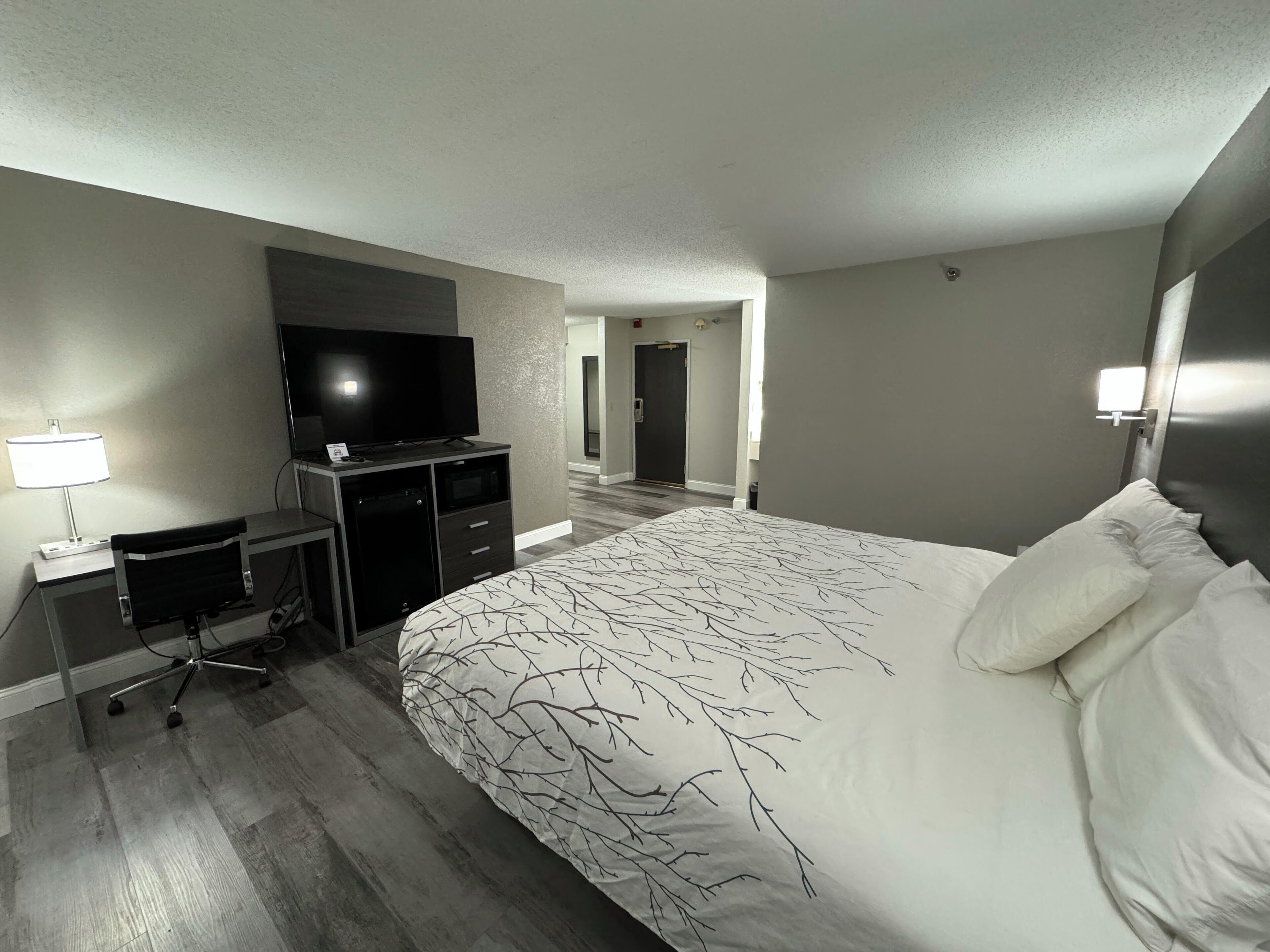 A hotel room with a large bed, a desk with a computer, a TV, and a lamp.