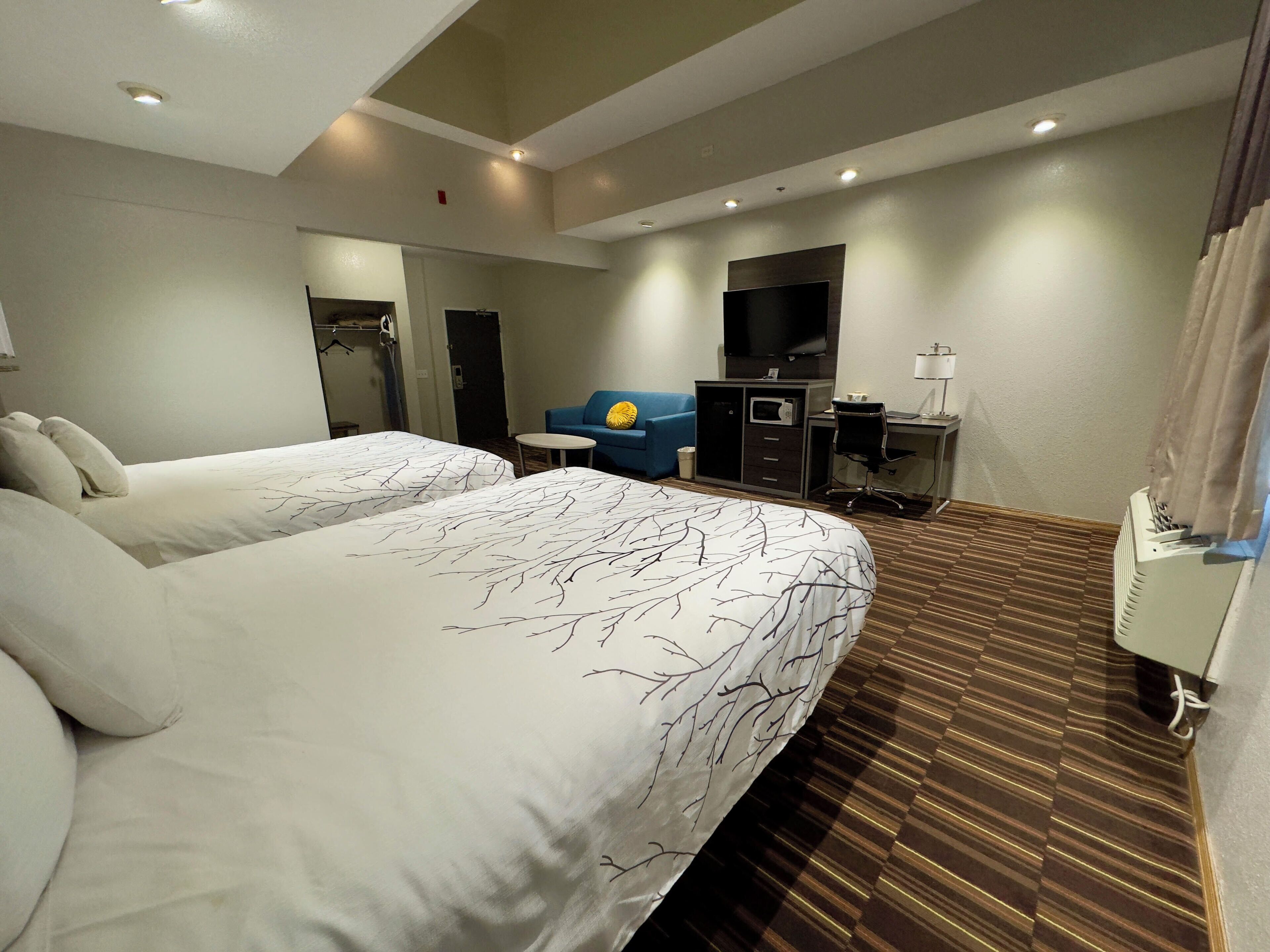 A hotel room with two beds, a desk, a TV, and a blue sofa.