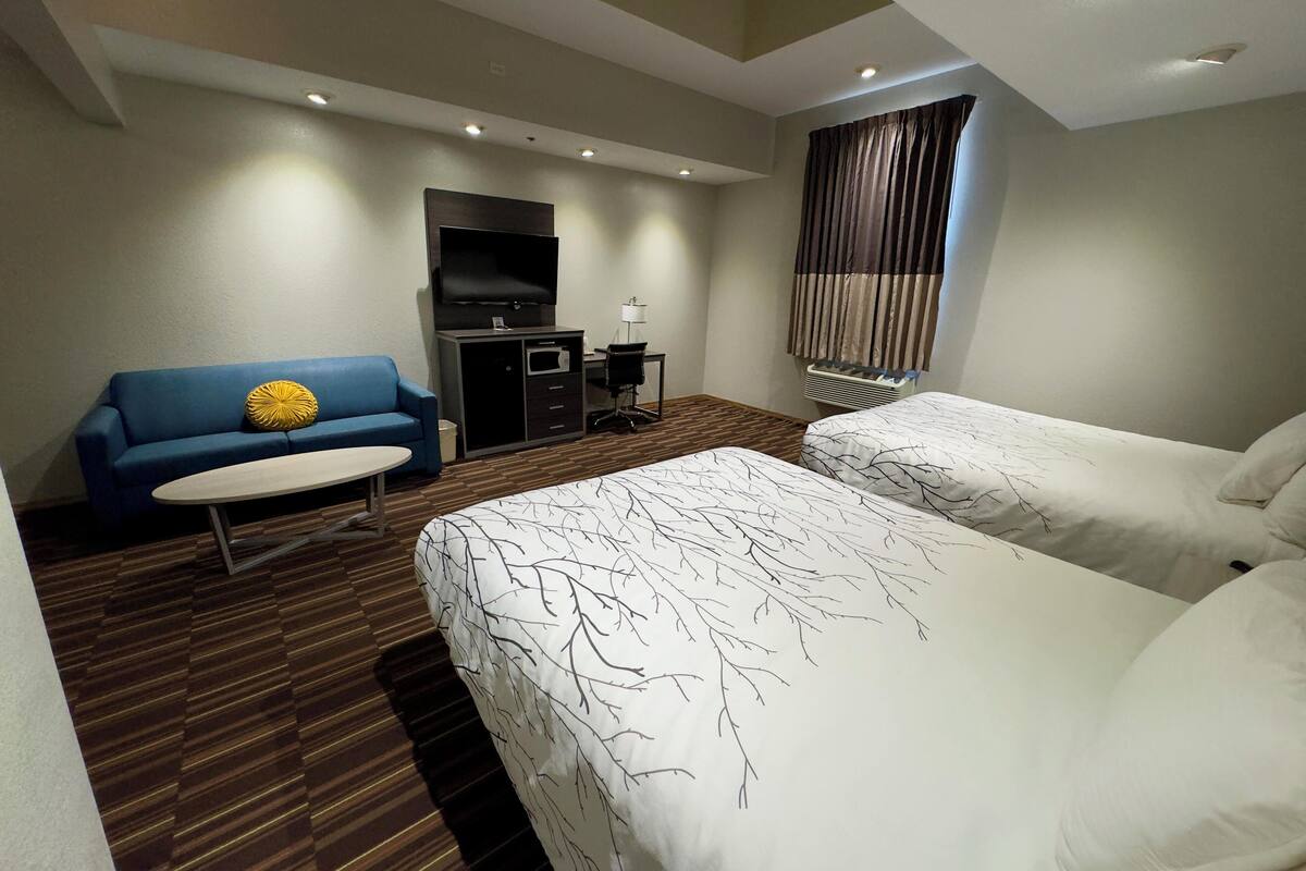A hotel room with two beds, a sofa, a TV, and a desk.