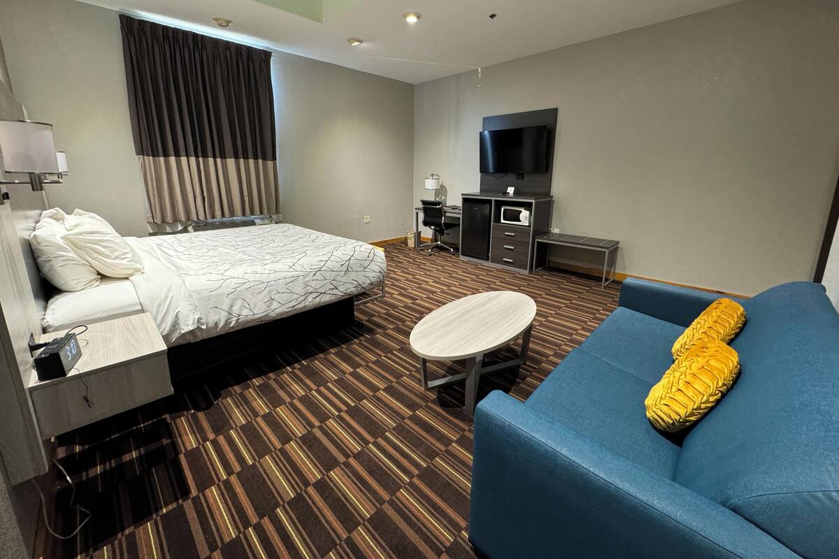 A hotel room with a bed, a sofa, a desk with a flat-screen TV, a microwave, and a small table.