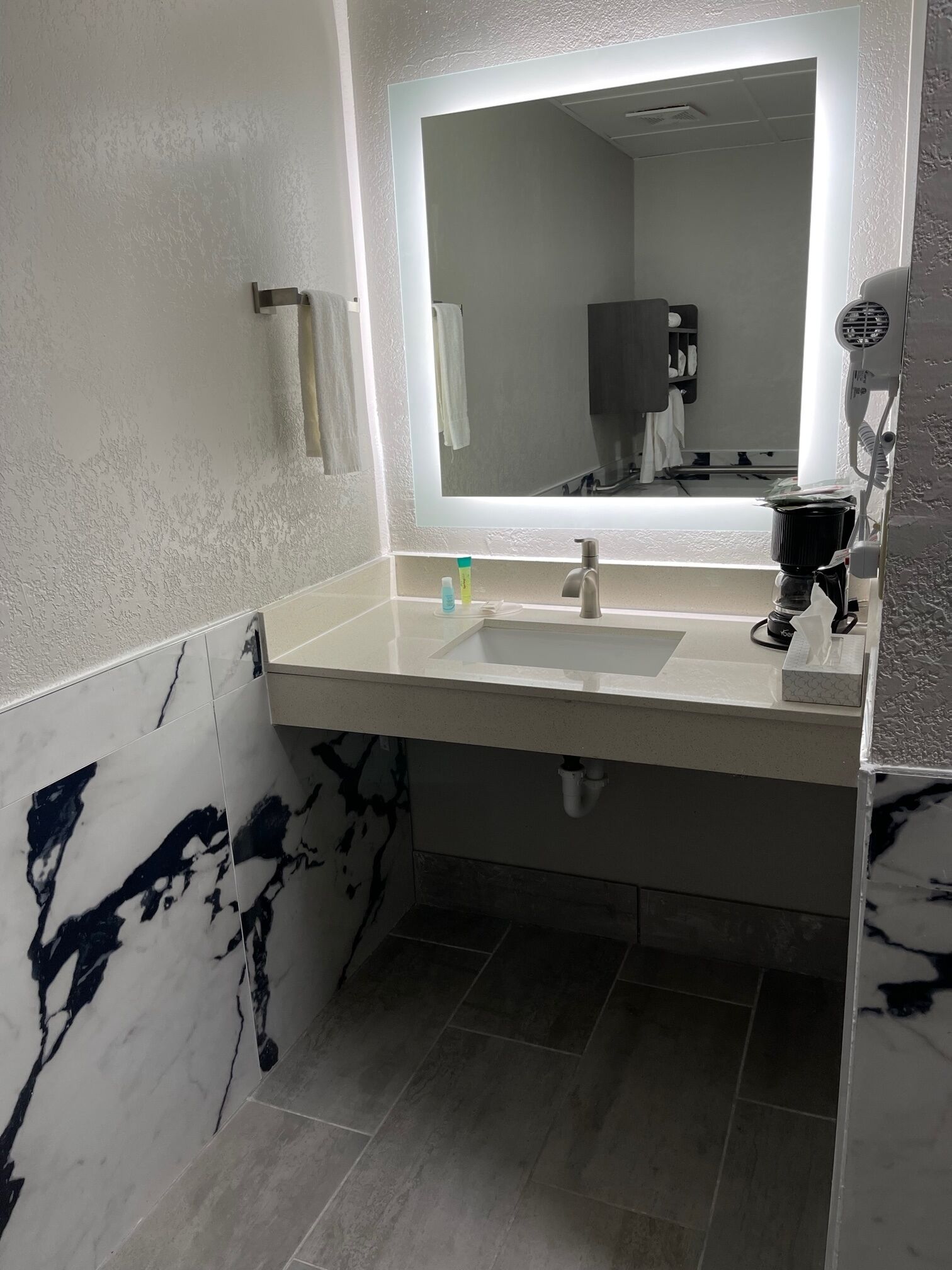 A bathroom with a white sink, a mirror, and a hairdryer on the wall.