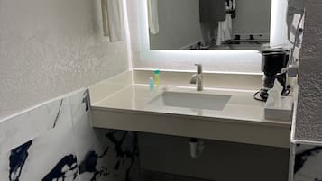 A bathroom with a white sink, a mirror, and a hairdryer on the wall.