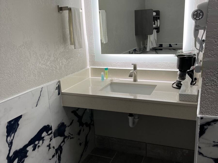 A bathroom with a white sink, a mirror, and a hairdryer on the wall.