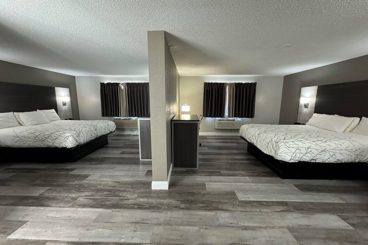 A hotel room with two beds, a desk, a chair, a lamp, and an air conditioning unit.