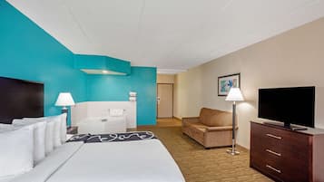 Una habitación de hotel con cama, sofá, televisor, escritorio y lámpara.