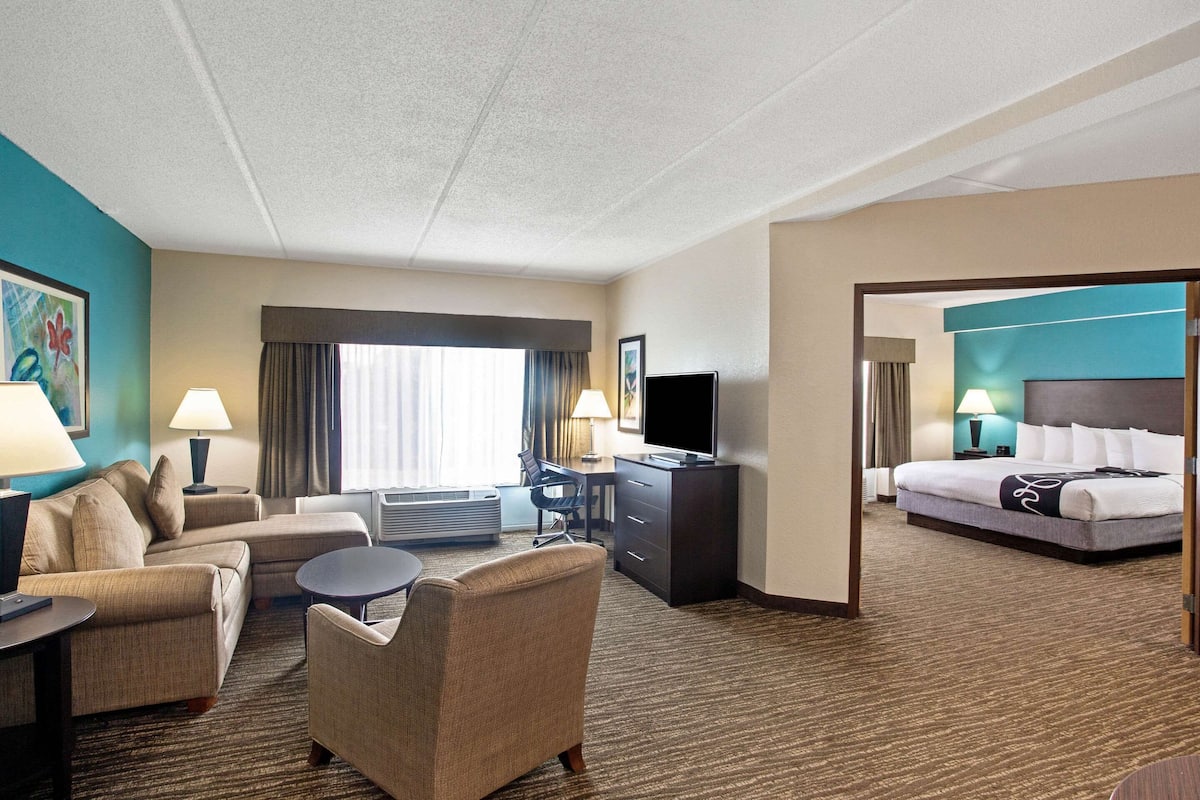 Una habitación de hotel con sofá, sillón, escritorio, televisión y cama.