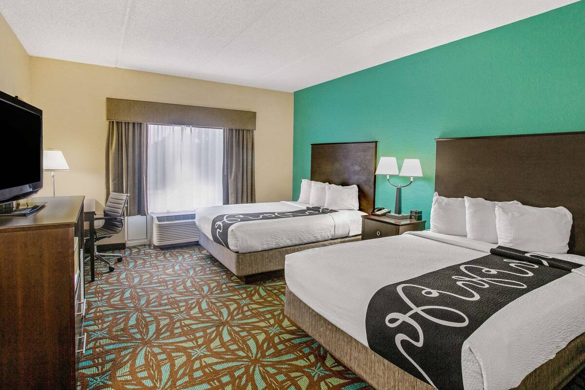 Habitación de hotel con dos camas, un escritorio, televisor y ventana con cortinas.