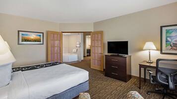A hotel room with a bed, a desk, a TV, a chair, and a bathroom visible through an open door.