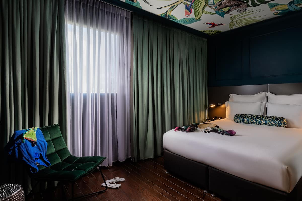 Une chambre d’hôtel avec un lit, une chaise, un bureau et une fenêtre avec des rideaux.