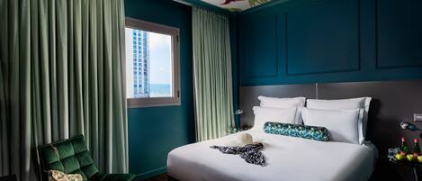 A hotel room with a large bed, a green chair, and a window with curtains.