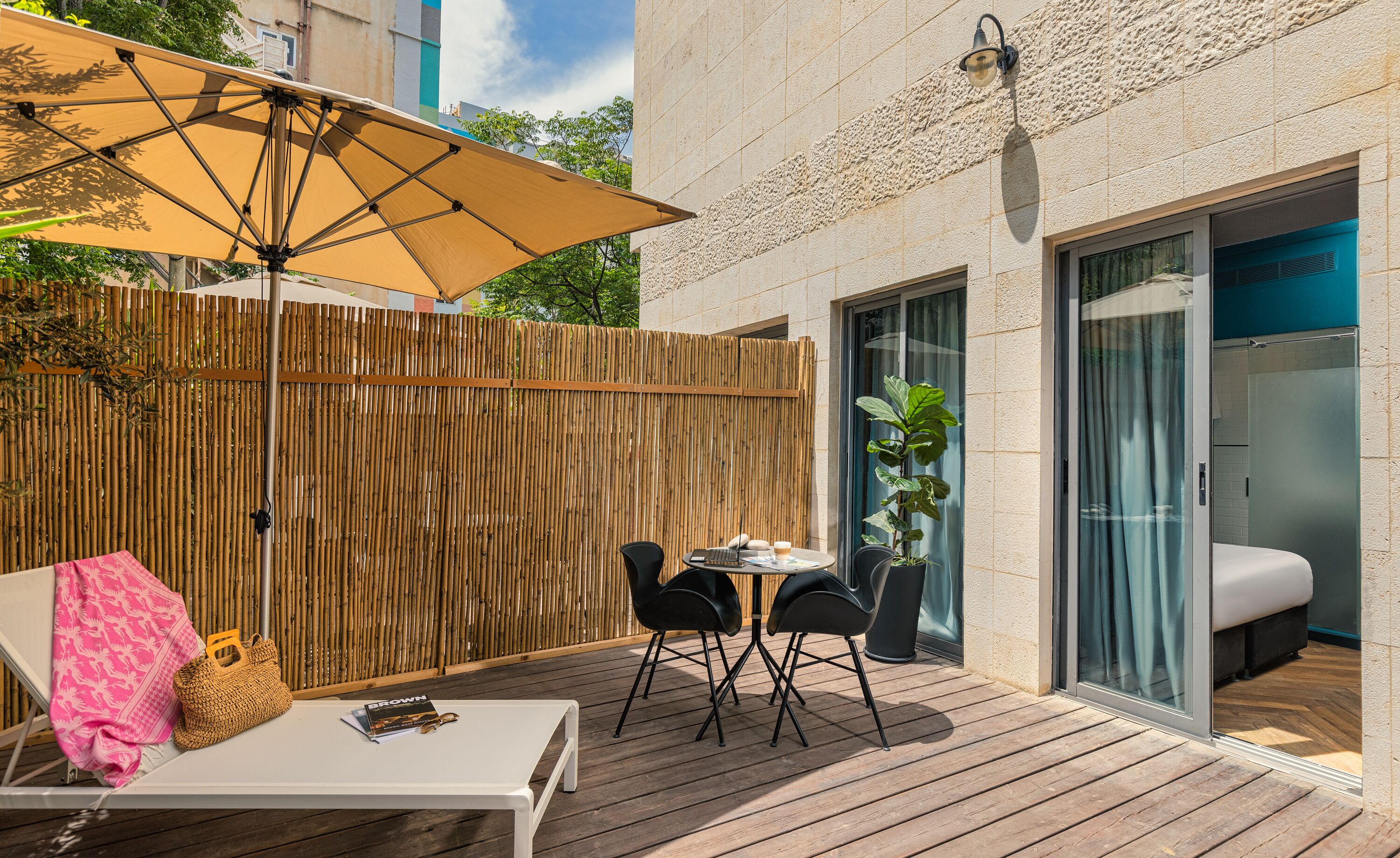 Terraza de madera con mesa, sillas, un paraguas grande y una valla de bambú.