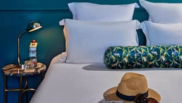 A bed with white linens, a straw hat, sunglasses, and a notebook on a teal-colored wall.