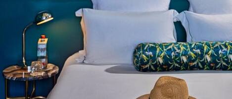 Een bed met witte lakens, een strohoed, zonnebril en een notitieboekje tegen een wand in teal.