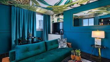 A teal-themed living room with a sofa, a coffee table with fruits, a TV, and a mirror on the wall.